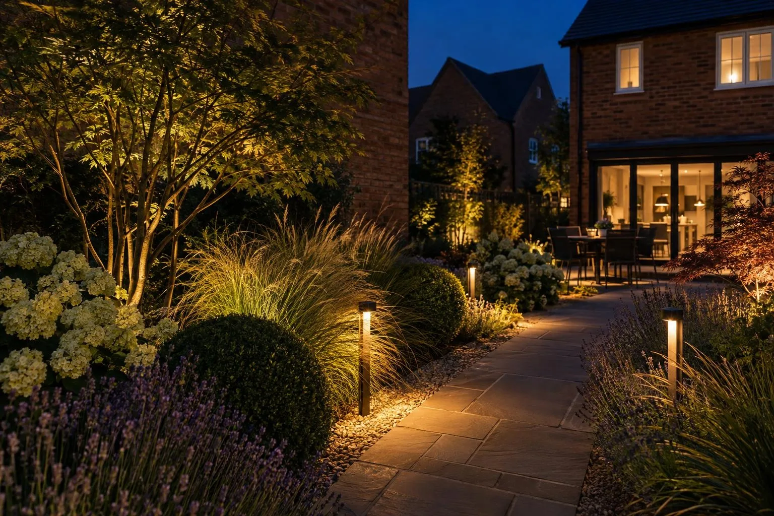 Low-voltage path lights along a garden path with uplit grasses at night, brick house garden Low-voltage path lights along a garden path with uplit grasses at night, brick house garden